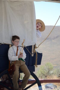 Two pioneer kids playing on a covered wagon